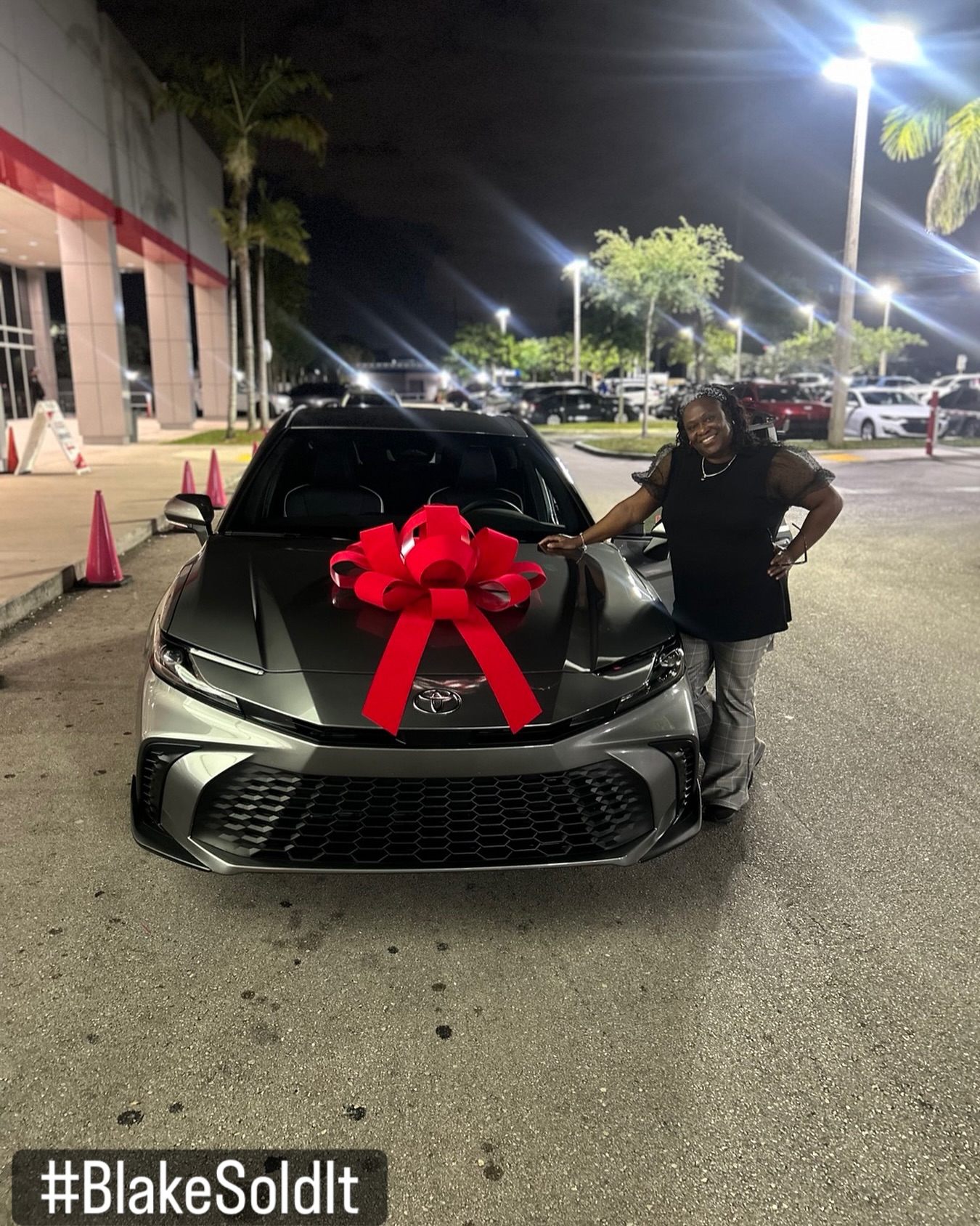 Client standing beside her new Toyota Crown with a red bow on the hood at night