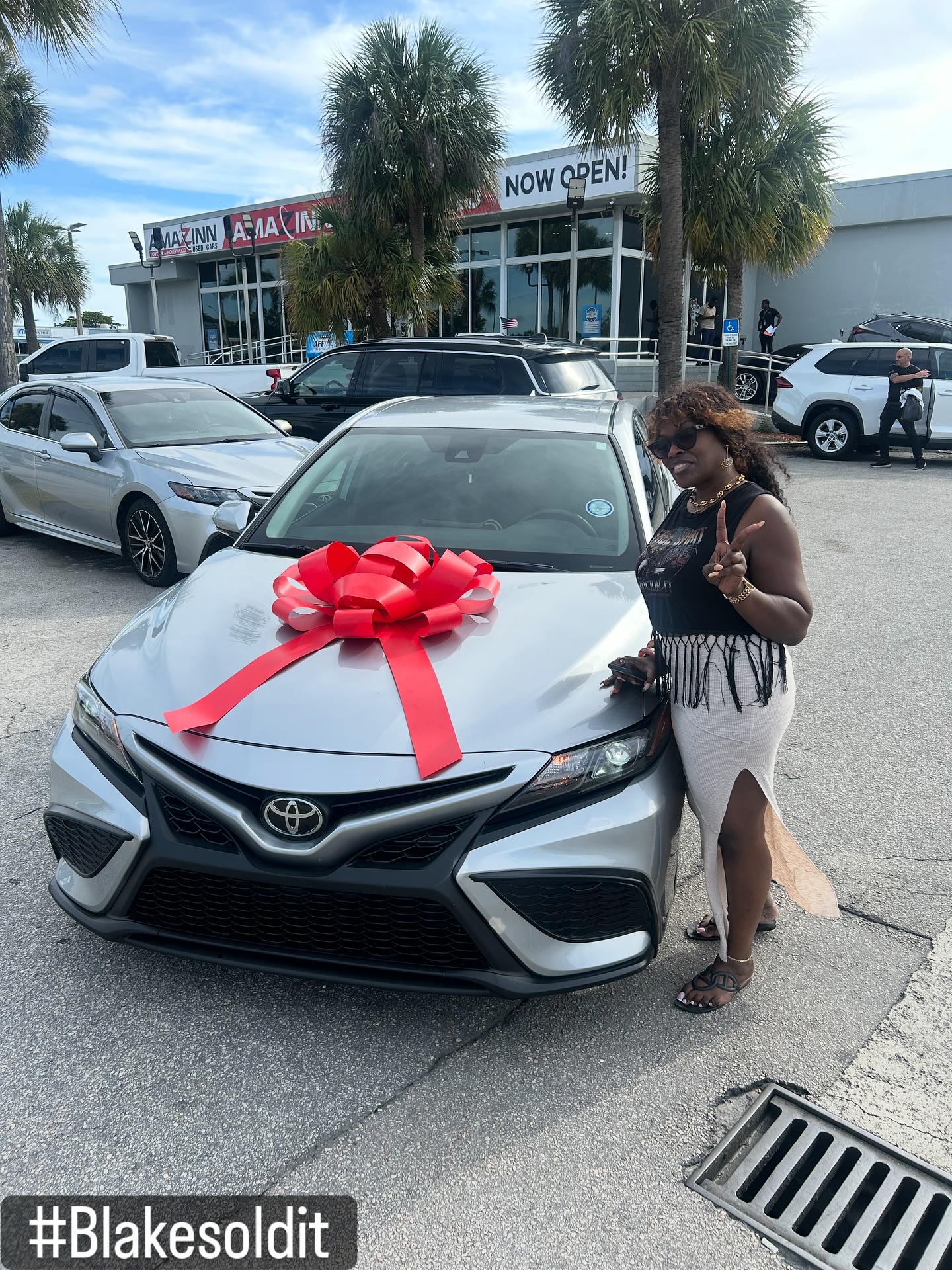 Client throwing a peace sign next to her new Toyota Camry with a red bow on the hood